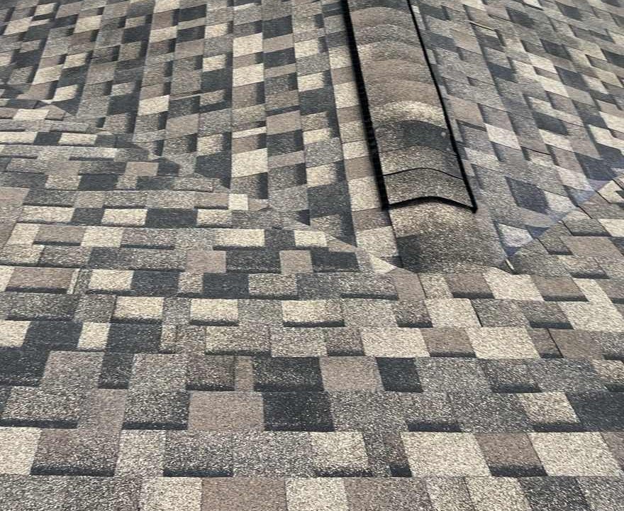 Cap shingles running up a hip where two planes of a tan, brown and charcoal architectural roof meet, the capped line rising away from the camera with the shingle surface falling off to either side