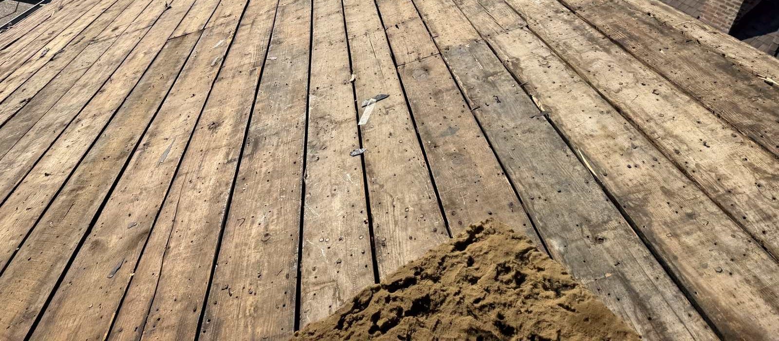 Original plank sheathing exposed after a tear off, with open gaps between the boards and rows of old nail holes across the wood