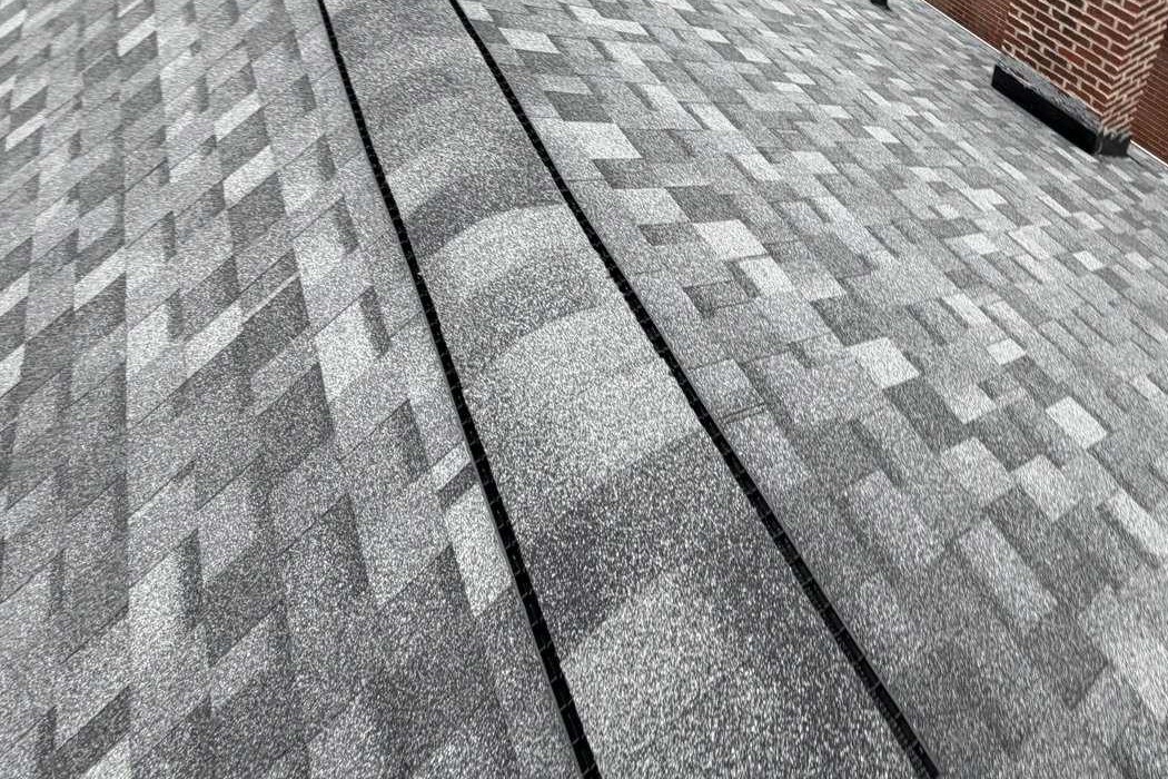 Grey architectural shingle courses running up to a ridge, showing the granule blend and the shading across the plane