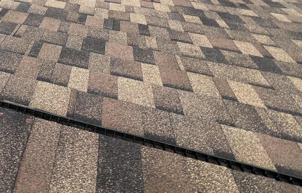 Architectural shingle courses in a tan and brown blend, with a black ridge vent strip running across the plane