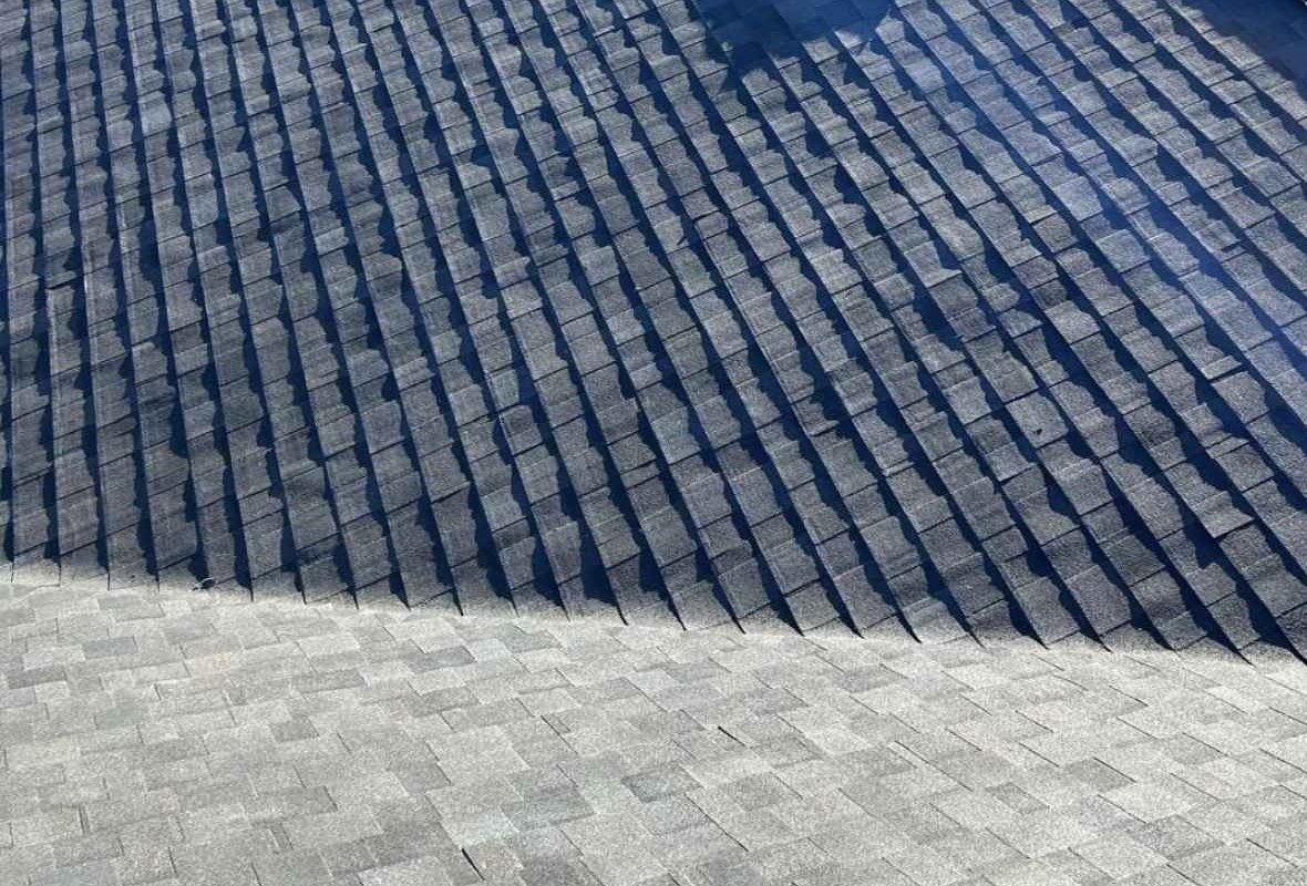 Dark shingle courses running down a steep roof plane to a break, where a lighter grey plane begins below
